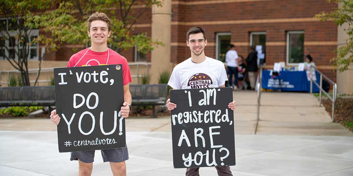2 young men holding voter registration signs