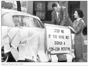 Man and woman standing near car with sign: Stop me if you have signed a Con Con petition"
